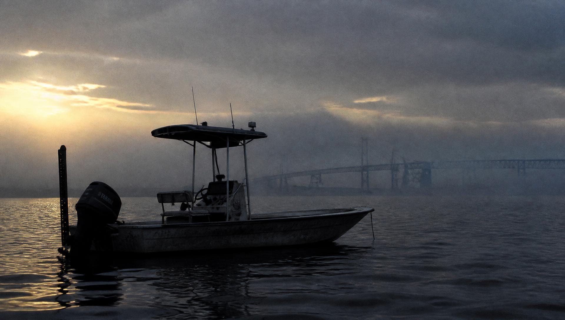 A center console skiff at dawn on the middle Chesapeake Bay with the Bay Bridge in the fog